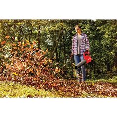 a woman standing in the leaves with a leaf blower