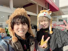 two people standing in front of a store with stuffed animals on their heads and one holding up the peace sign