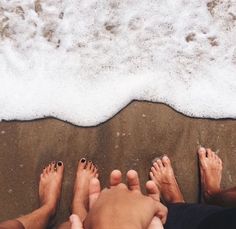 three people standing on the beach with their feet in the water