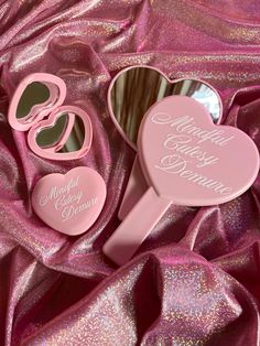 two pink heart shaped mirrors sitting next to each other on a purple satin covered surface