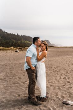 a man and woman standing on top of a sandy beach