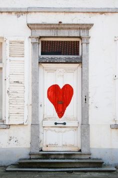 a red heart painted on the front door of an old building with white shutters