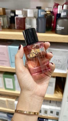 a woman holding up a bottle of pink perfume in front of shelves with other items