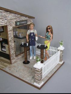 two dolls are standing in front of a doll house with a coffee table and bar