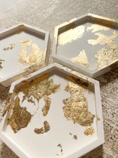 three trays with gold paint on them sitting on a tablecloth covered surface,