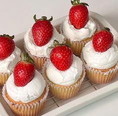 cupcakes with white frosting and strawberries on top are sitting on a tray