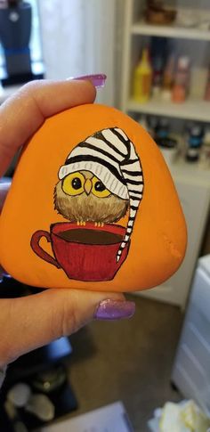 a hand holding an orange painted rock with a coffee cup and zebra print hat on it