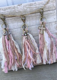 three tassels hanging from a string on a wooden board with lace and beads