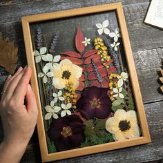 a person is holding up a painting with flowers in it on a table next to pine cones and an acorn