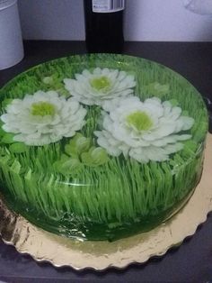 a green cake with white flowers on it sitting on a table next to a bottle