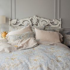 a bed with an ornate headboard and blue comforter in a gray room next to a lamp