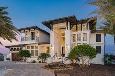 a large white house with lots of windows and palm trees in front of it at dusk