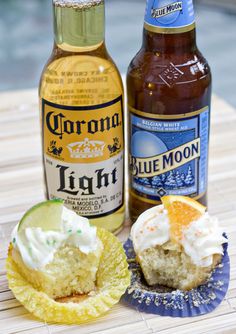 two beer bottles sitting next to cupcakes on a table