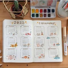 an open planner book sitting on top of a wooden table next to markers and pens