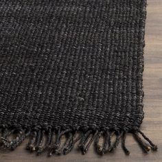 a black rug with tassels is laying on a wooden floor