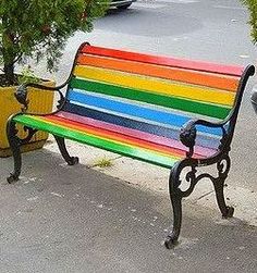 a rainbow colored bench sitting next to a potted plant on the side of a street