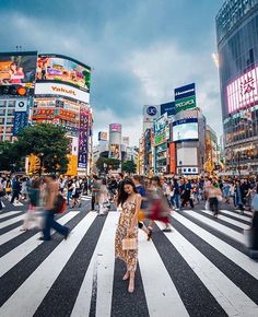 a woman standing in the middle of a crosswalk with lots of people walking around