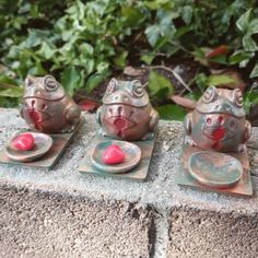 three metal frog figurines sitting next to each other on top of a stone slab