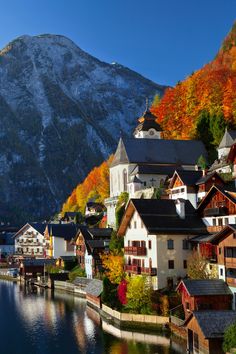 a village on the shore of a lake in front of a mountain covered with autumn foliage