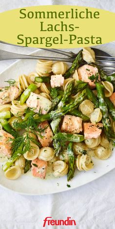 a white plate topped with pasta and asparagus covered in salmon sauce next to a fork