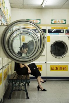 a woman sitting on a bench in front of a washing machine with her reflection in the window