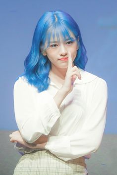 a woman with blue hair is posing for the camera while holding her finger to her lips