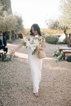 a woman in a white dress walking down a path with flowers on her head and holding a basket