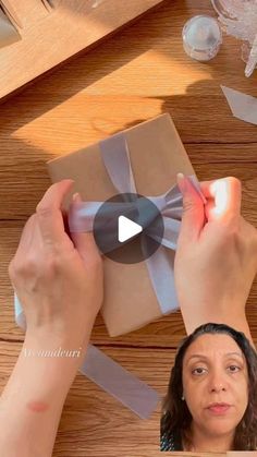 a woman opening a gift box on top of a wooden table next to other items