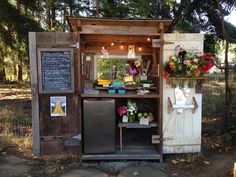 an old outhouse with flowers and plants on the outside, sitting in front of trees