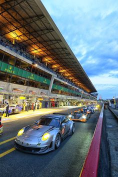 a group of cars driving down a street next to a race track at night time