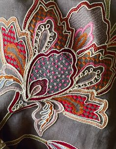 closeup of an embroidered fabric with flowers and leaves in red, pink, blue, orange and grey colors