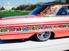 an old pink car with flowers painted on it's side and the capitol building in the background