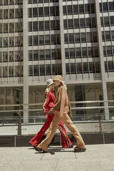 two people walking down the sidewalk in front of tall buildings