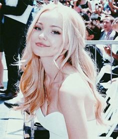 a beautiful young blonde woman sitting on top of a white chair in front of a crowd