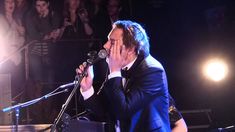 a man in a suit and tie holding his face to his mouth while singing into a microphone