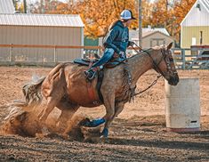 a woman riding on the back of a brown horse next to a white barrel in an arena