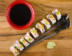 sushi on a wooden table next to a cup of black sauce and chopsticks