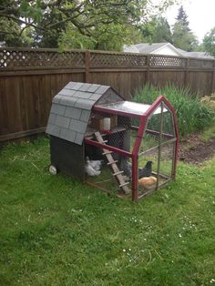 a chicken coop with chickens in it on the grass next to a fence and trees