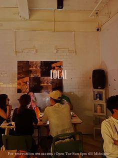 several people sitting around a table in a room with white walls and exposed ceilinging