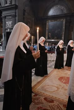 several women in nun dresses holding candles and standing next to each other on a rug