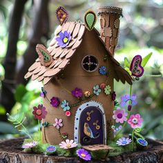 a small house made out of cardboard with flowers and leaves on the outside, sitting on a tree stump