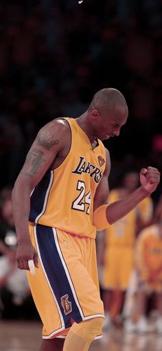 a basketball player in yellow jersey standing on the court with his fist up and looking down