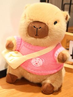 a teddy bear wearing a pink sweater and holding a yellow ribbon around its neck, sitting on a wooden floor