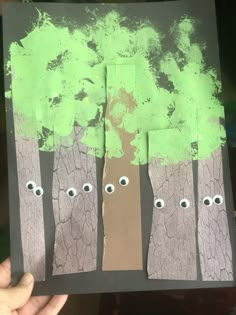 someone is holding up a piece of paper with trees and eyes painted on it in front of them