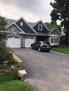 a black car parked in front of a large house with two garages on each side