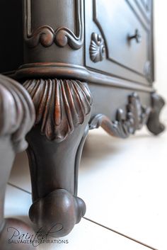 an ornate wooden cabinet with metal handles and knobs on the door handle, in front of a white tile floor