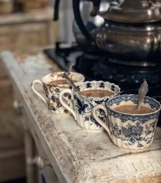 three coffee mugs sitting on top of a wooden table next to a tea pot