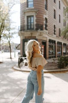 a woman standing on the sidewalk in front of a building wearing high waist jeans and a cropped top