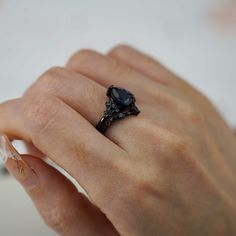 a woman's hand holding a ring with a black diamond on it and the middle finger