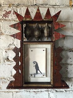 an old wooden frame hanging on a brick wall with vases in the back ground